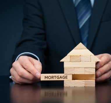 a man in a suit holding a wooden block with a house on it.