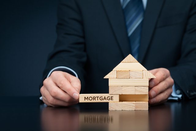 a man in a suit holding a wooden block with a house on it.