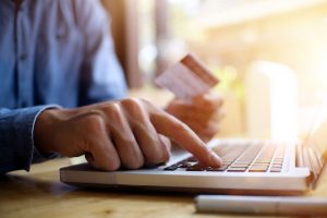 a person using a laptop computer while holding a credit card.