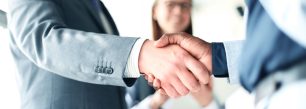 two business people shaking hands in front of a woman.