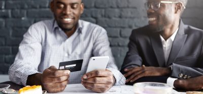 two men sitting at a table looking at a cell phone.