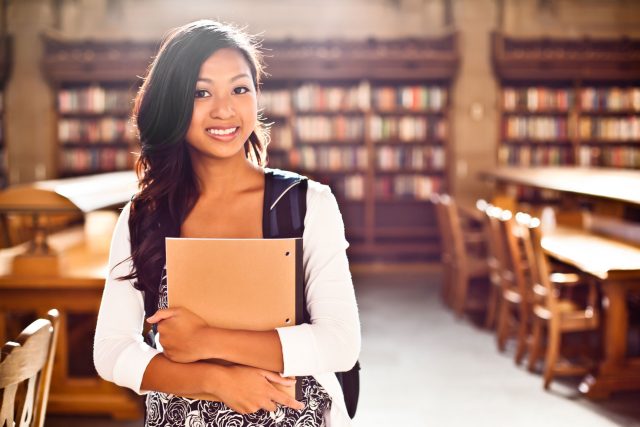 a woman standing in a library holding a folder.